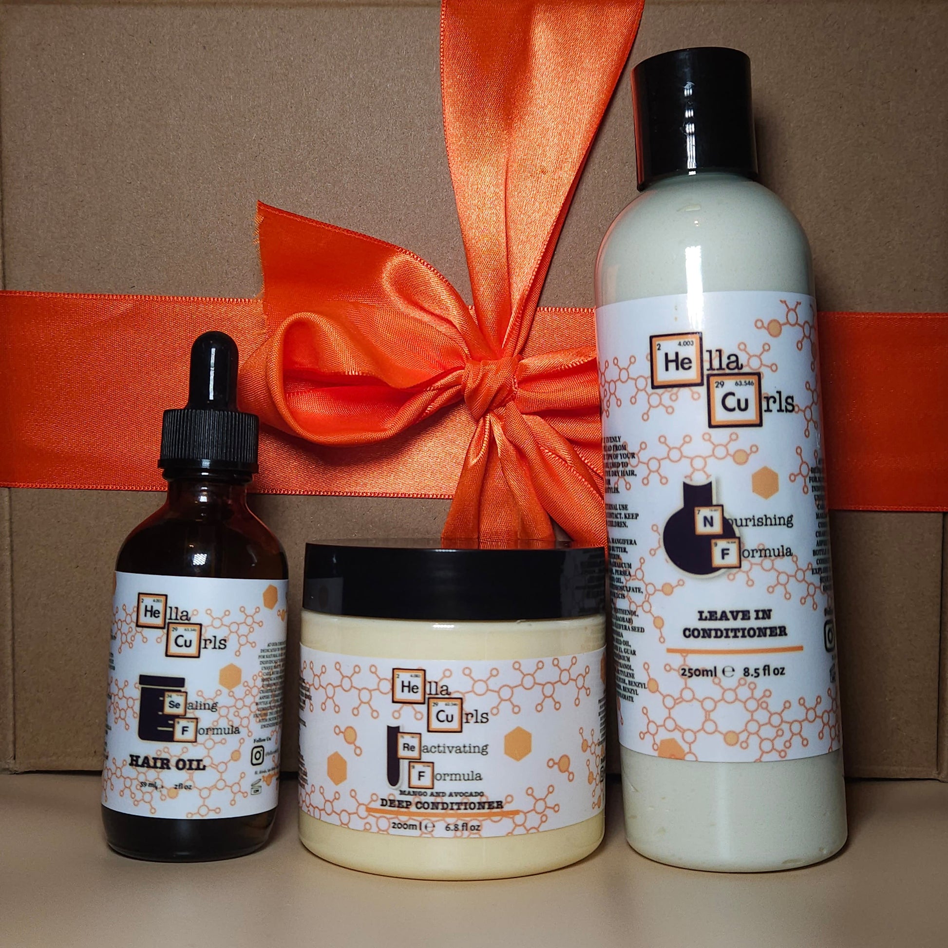 Set of Hella Curtis hair care products with a decorative orange bow on a brown box.