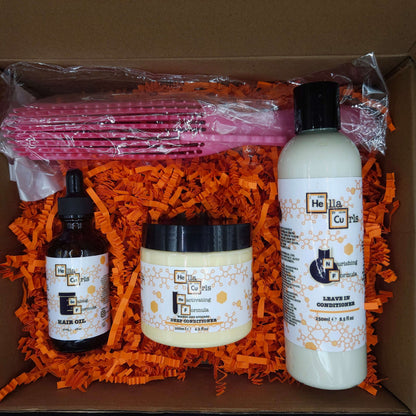 Set of hair care products including bottles and a jar on orange shredded paper with a pink comb inside a cardboard box.